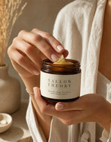 Hands scooping Tallow Theory balm from an amber glass jar in natural light
