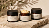 Three Tallow Theory balm jars grouped on a stone surface